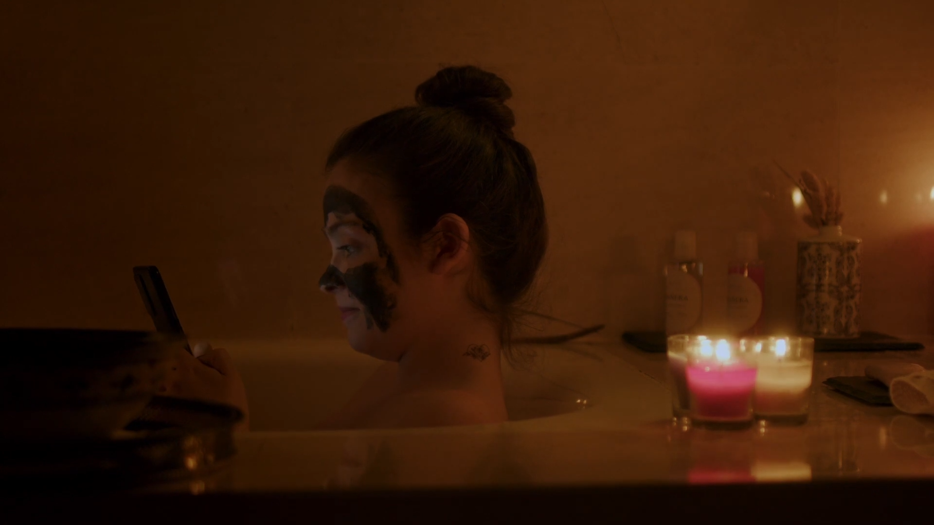 Mujer joven con una mascarilla facial relajándose en la bañera a la luz de las velas, reflejando un momento de calma y autocuidado en 'Siempre me acabo encontrando a mi misma en la bañera'.